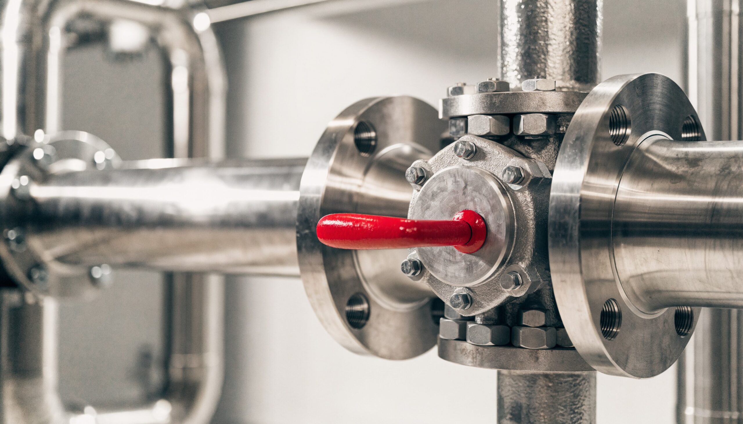 Industrielle Absperrarmatur mit Flanschanschluss zwischen Edelstahlrohren und rotem Handhebel