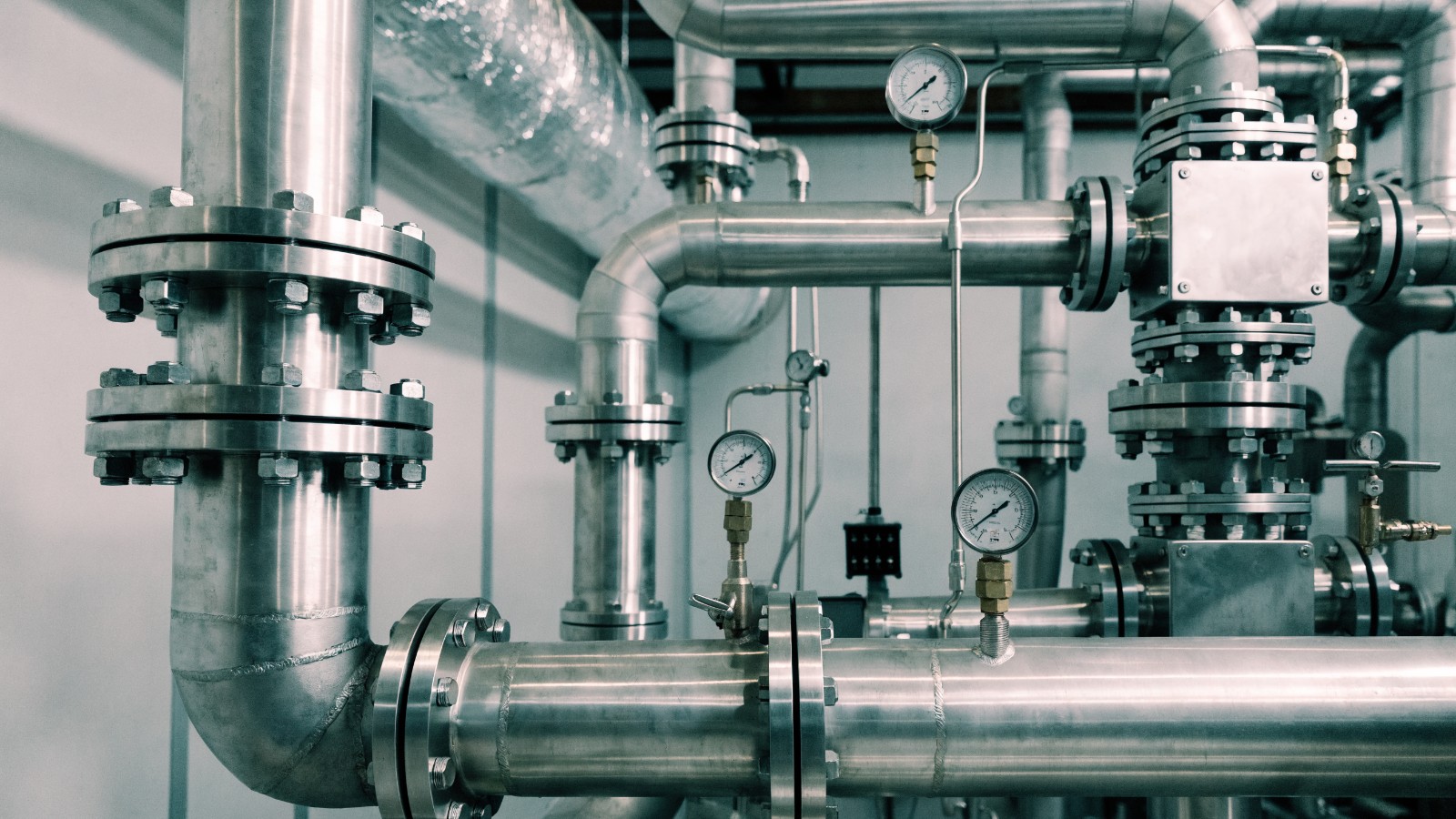 Industrielle Rohrleitungen mit Armaturen, Ventilen, Flanschen und Manometern aus Edelstahl in einer Anlage