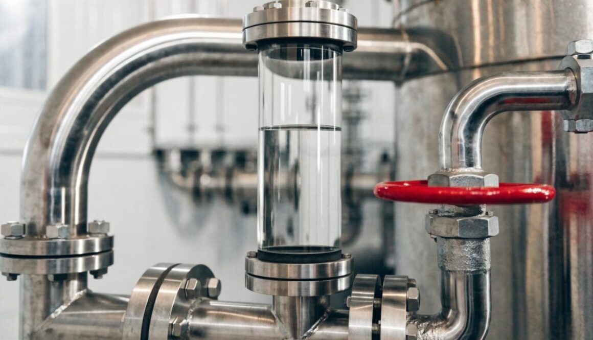 Industrieller Wasserstandsanzeiger als Schauglas an Edelstahlrohren mit sichtbarem Wasserstand und rotem Absperr-Handrad